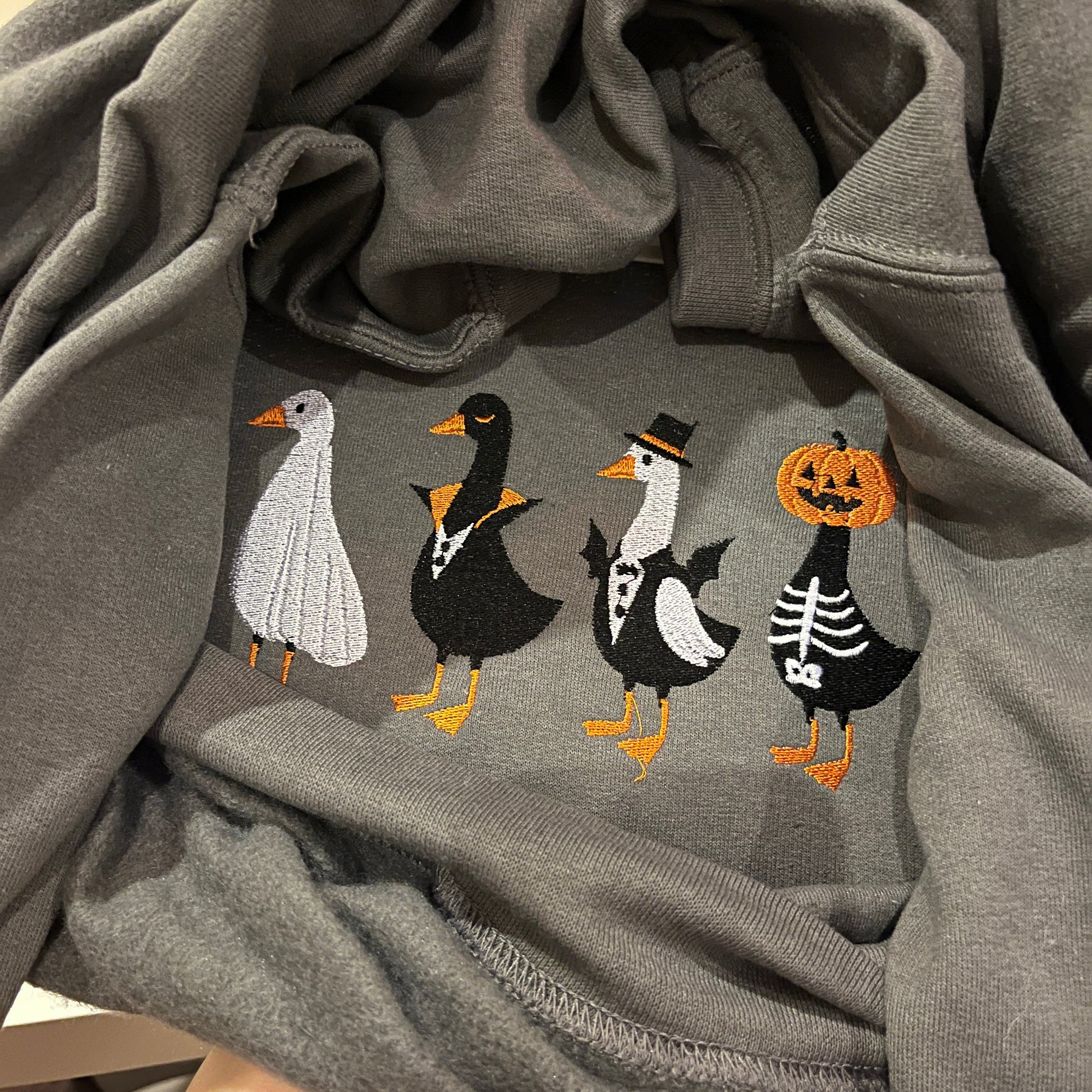 Gray sweatshirt with Halloween-themed embroidery of ghosts and pumpkins.
