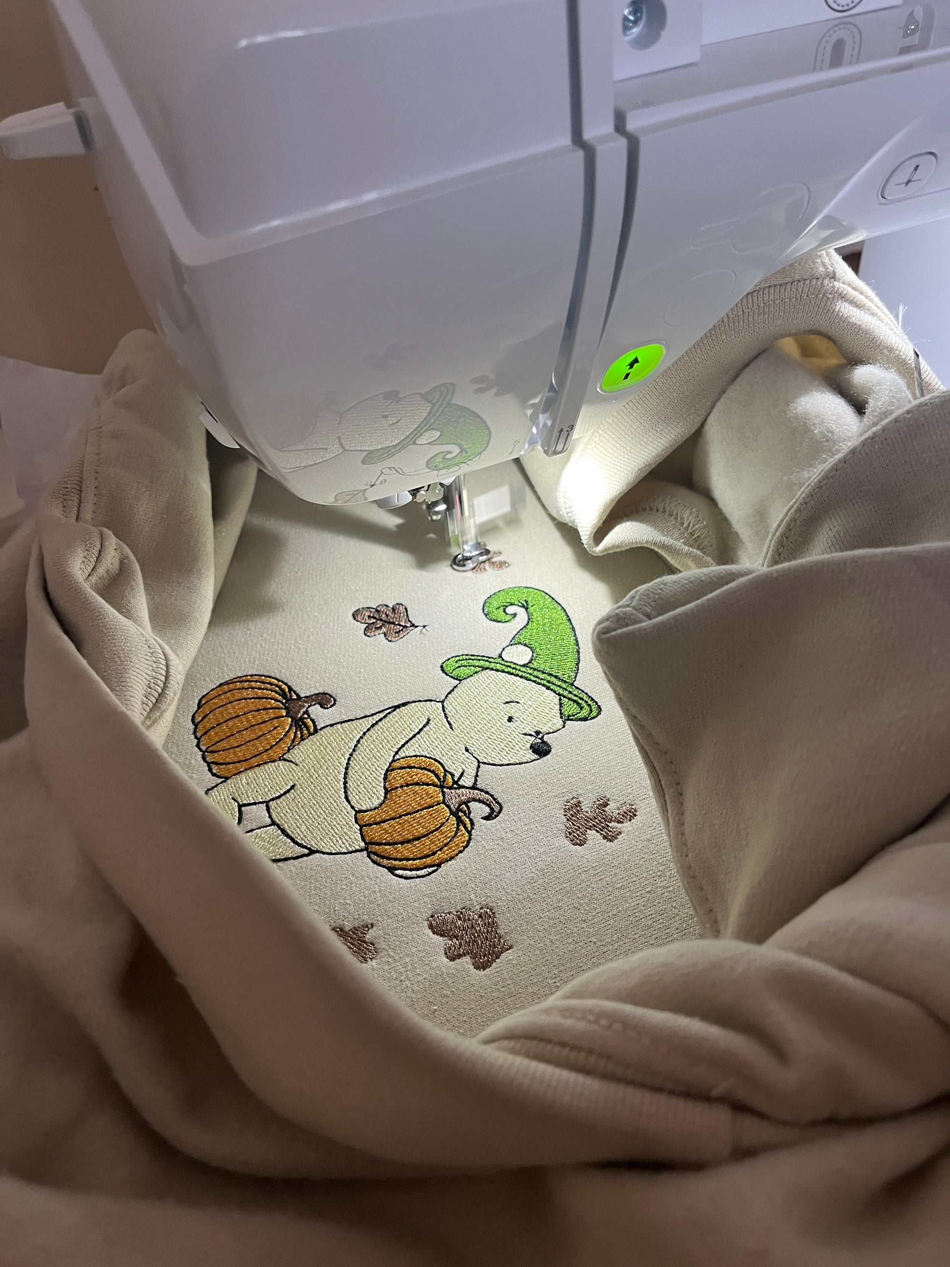 Close-up of a beige embroidered sweatshirt of a  cartoon bear and pumpkin design
