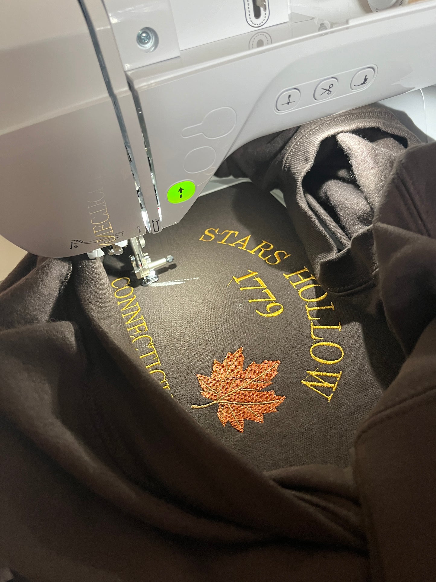 Embroidery machine with a piece of fabric featuring 'Stars Hollow 1779' and a maple leaf design.
